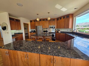 Cocina moderna con encimeras de granito, electrodomésticos de acero inoxidable, armarios de madera y una isla grande con taburetes de bar.