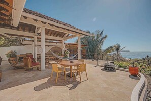 Eine Terrasse im Freien mit einem runden Tisch und Stühlen, einer Hängematte und einer Feuerstelle.
