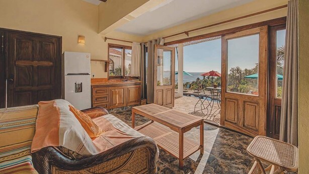 A cozy room with a sofa, a table, a refrigerator, and a view of the outdoors. - Villa Catalina - Pool - OceanViews - 5 King Suites (San Francisco)