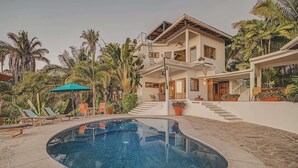 A two-story house with a swimming pool, surrounded by palm trees and a covered patio area. - Villa Catalina - Pool - OceanViews - 5 King Suites (San Francisco)