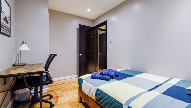 A bedroom with a bed, a desk with a chair, a lamp, and a wardrobe. - Spacious 4-bedroom apartment in tranquil New York with AC (New York)