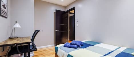 A bedroom with a bed, a desk with a chair, a lamp, and a wardrobe.