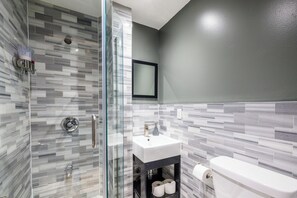 Un baño moderno con cabina de ducha de vidrio, un lavamanos blanco y un inodoro.