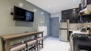A modern kitchen with a flat-screen TV, a refrigerator, a microwave, and a stove. There is a bench with stools and a door leading to another room. - Spacious 4-bedroom apartment in tranquil New York with AC (New York)