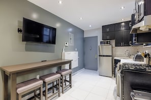 A modern kitchen with a flat-screen TV, a refrigerator, a microwave, and a stove. There is a bench with stools and a door leading to another room. - Spacious 4-bedroom apartment in tranquil New York with AC (New York)