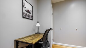 A small office space with a wooden desk, a chair, a desk lamp, and a framed picture on the wall. - Spacious 4-bedroom apartment in tranquil New York with AC (New York)