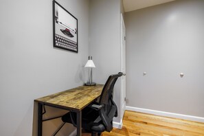 A small office space with a wooden desk, a chair, a desk lamp, and a framed picture on the wall. - Spacious 4-bedroom apartment in tranquil New York with AC (New York)
