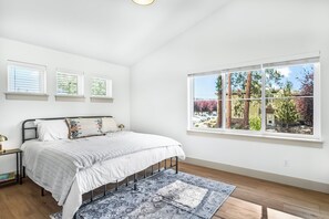 Une chambre à coucher avec un lit, une fenêtre donnant sur des arbres et une table de chevet avec une lampe.