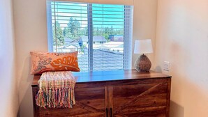 Un aparador de madera con cajones, una ventana con persianas y una lámpara encima.