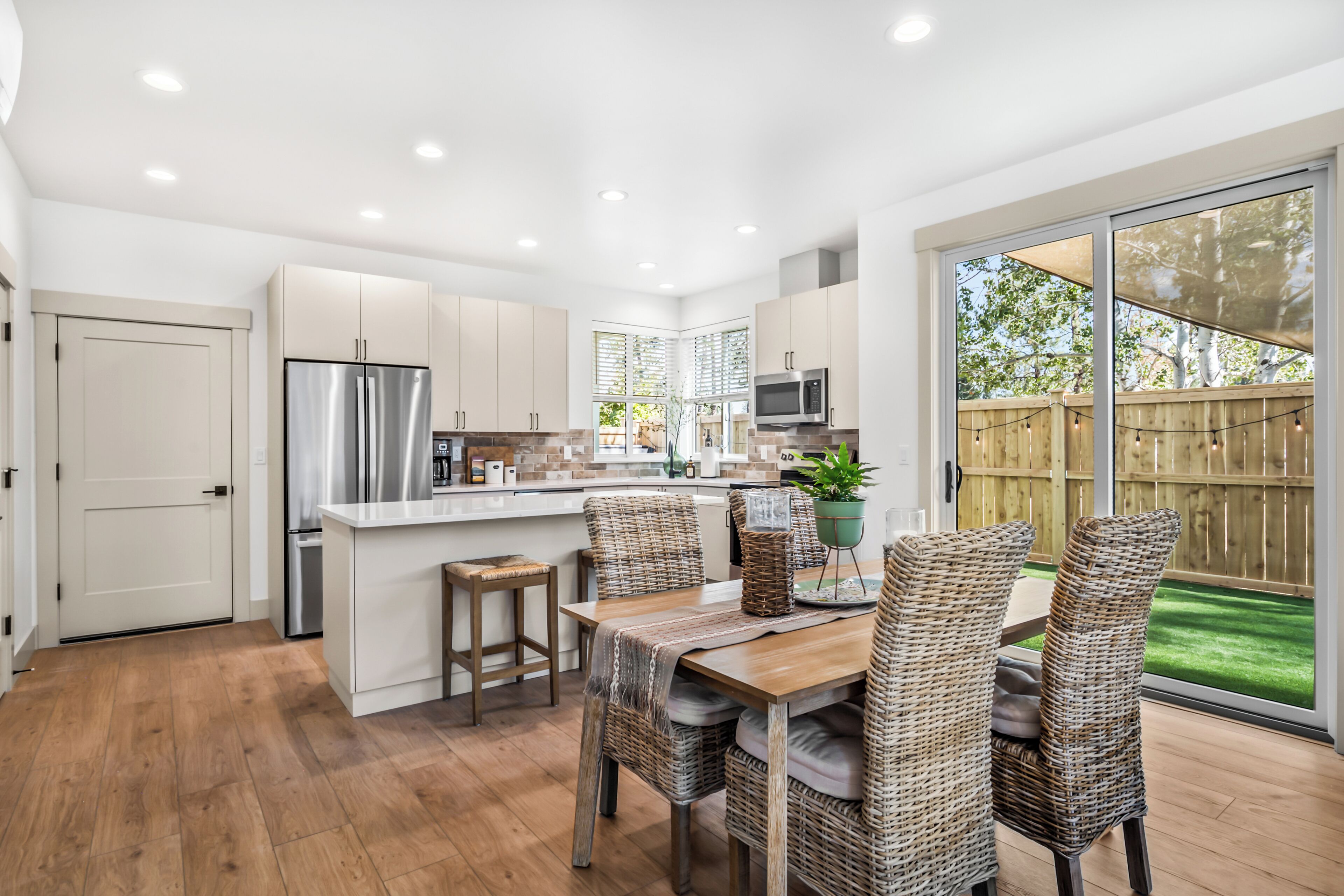 A modern kitchen with a central island, wooden flooring, and a dining area with wicker chairs.