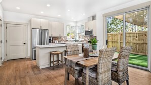 A modern kitchen with a central island, wooden flooring, and a dining area with wicker chairs. - NEW Downtown Sisters Luxe Retreat with Hot Tub + Firepit (Sisters)