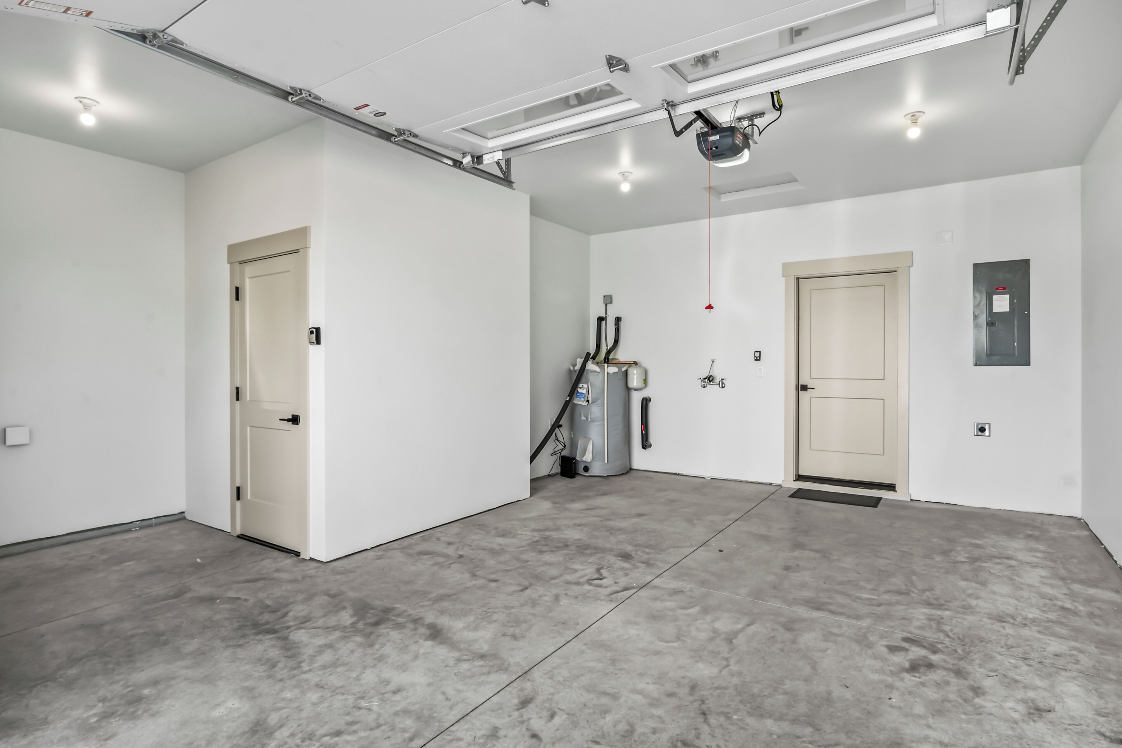 A spacious, well-lit industrial-style room with concrete flooring, two doors, and visible ceiling-mounted equipment.