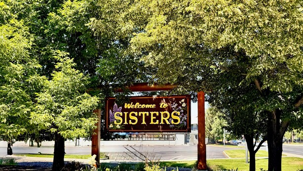 Letrero de bienvenida que dice 'SISTERS', con un jardín al frente.
