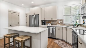 Una cocina moderna con armarios blancos, un refrigerador de acero inoxidable, horno empotrado y una isla grande con taburetes de bar.