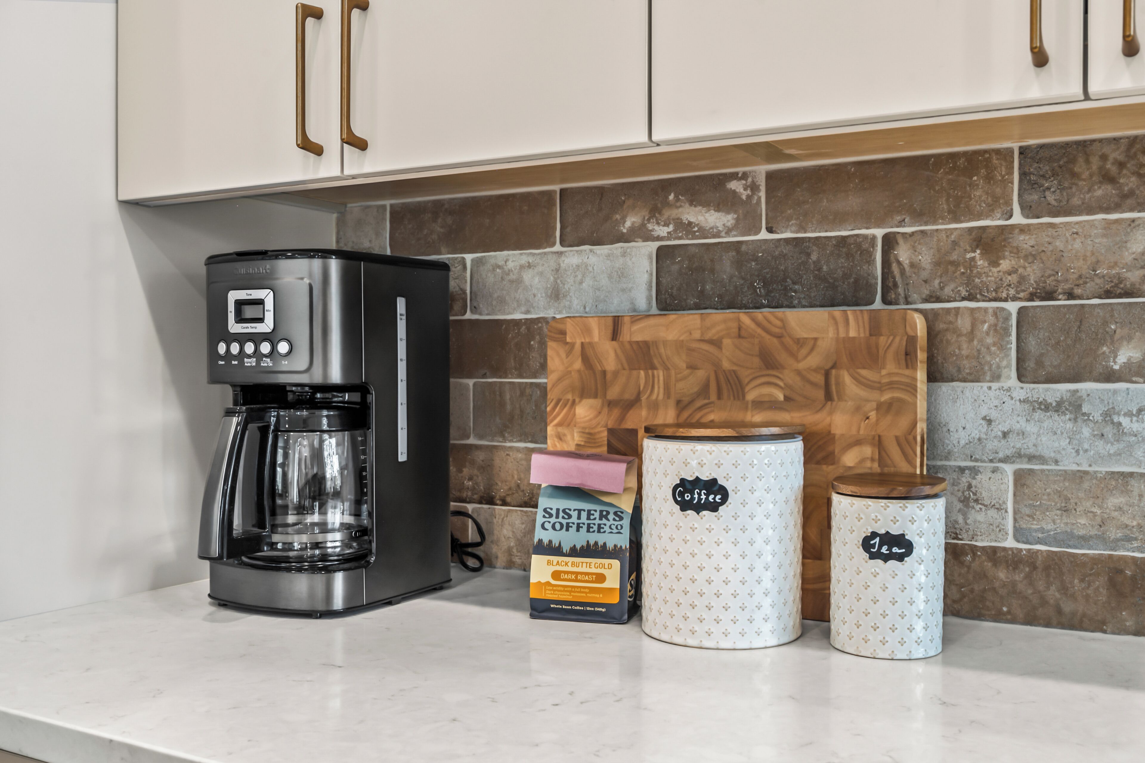 Een keuken met een koffiezetapparaat, een snijplank en twee bakken met de tekst 'Koffie' en 'Thee'.