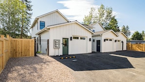A two-story building with a garage, a gravel driveway, and a wooden fence. - NEW Downtown Sisters Luxe Retreat with Hot Tub + Firepit (Sisters)