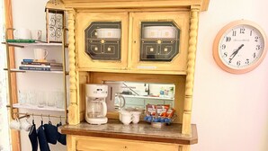 Une cuisine au style rétro, avec une machine à café, une horloge et une étagère remplie de livres et de verres.
