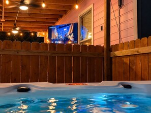 Un bain à remous avec une terrasse en bois et un écran de télévision en arrière-plan.