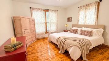 Een slaapkamer met een houten vloer, een bed met witte beddengoed, een nachtkastje met een lamp en een kledingkast.