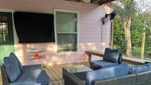 Une terrasse extérieure aménagée avec des meubles en osier, une table et un téléviseur fixé au mur.