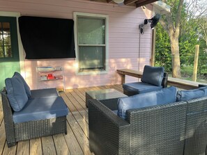 An outdoor patio with wicker furniture, a table, and a TV mounted on the wall. - Downtown Blush Bungalow and Hot Tub (Boerne)