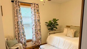 Une chambre à coucher avec un lit, une chaise, une plante et une fenêtre avec des rideaux.