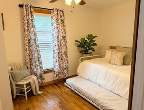 A bedroom with a bed, a chair, a plant, and a window with curtains. - Downtown Blush Bungalow and Hot Tub (Boerne)