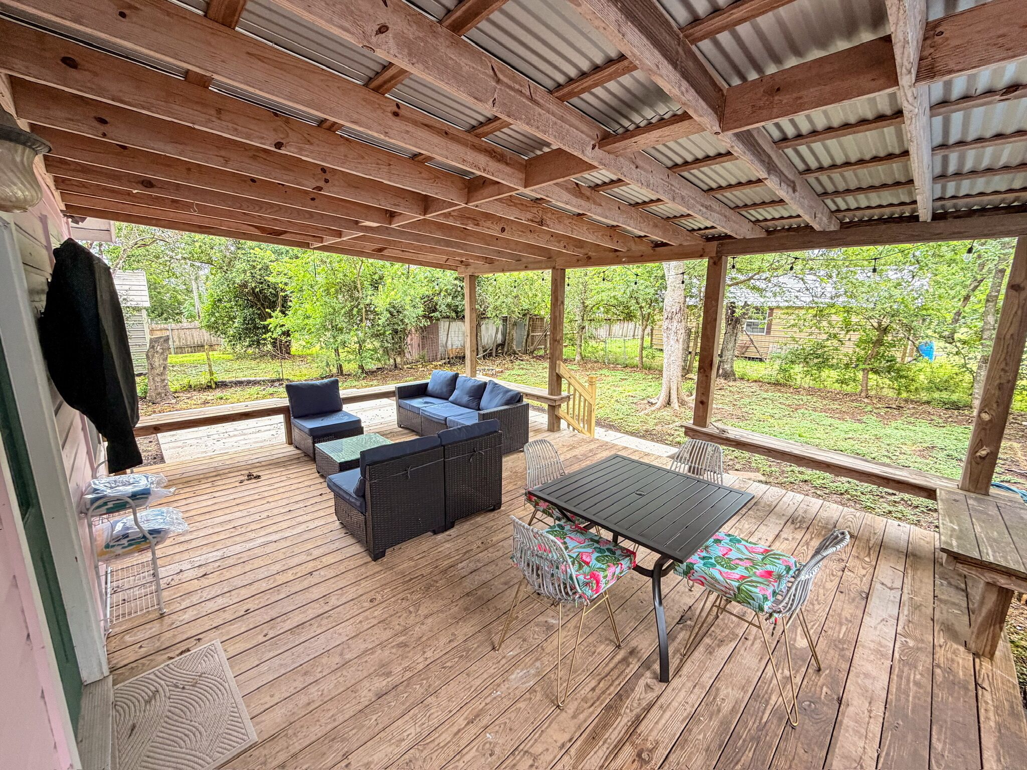 A covered outdoor patio with wooden flooring, a table, and two sofas.