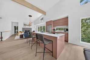 A modern kitchen with a large island, bar stools, and a view of the outdoors. - New Home + Guest House on Bike Trail (Bella Vista)