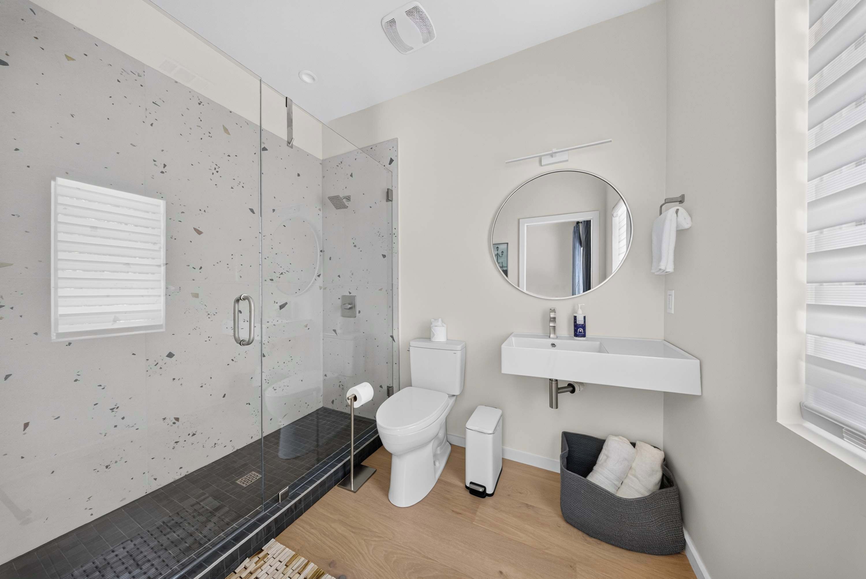 A modern bathroom with a glass shower enclosure, a toilet, a sink with a mirror, and a towel rack.