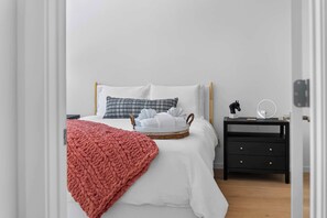 A neatly made bed with a white comforter, a red blanket, and a basket of folded towels. - New Home + Guest House on Bike Trail (Bella Vista)