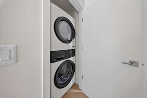 A laundry room with two front-loading washing machines, a door with a handle, and a light switch on the wall. - New Home + Guest House on Bike Trail (Bella Vista)