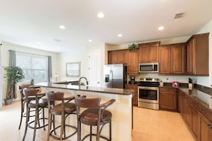 A modern kitchen with a central island, stainless steel appliances, wooden cabinets, and bar stools. - Luxury Dreams Disney Home Private Pool Spa Gameroom (Kissimmee)