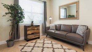 Ein Wohnzimmer mit einer Couch, einer Holzkommode, einem Blumentopf, einem Teppich und einem großen Spiegel an der Wand.