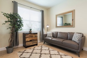 Ein Wohnzimmer mit einer Couch, einer Holzkommode, einem Blumentopf, einem Teppich und einem großen Spiegel an der Wand.