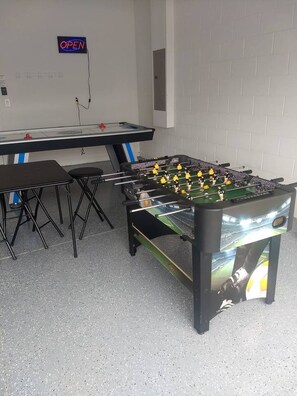 A foosball table in a room with a white brick wall, a table with chairs, and a neon 'OPEN' sign. - Luxury Dreams Disney Home Private Pool Spa Gameroom (Kissimmee)