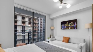Quarto de hotel moderno com uma cama grande, um sofá, vista para a cidade e uma varanda com vista para a construção.