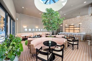 Ein moderner Loungebereich mit Sitzgelegenheiten, einem zentralen Baum und einer Bar mit Regalen.