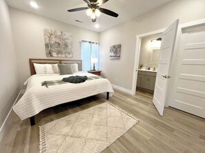 A bedroom with a bed, a ceiling fan, a nightstand, a bathroom visible through an open door, and a hallway. - Blue Horizon-Panoramic Lake View on Indian Point--Pools-1 mile to Silver Dollar (Branson)