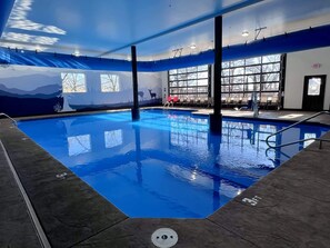 Une piscine intérieure à l’eau claire, une fresque murale et un espace détente avec des chaises.