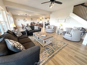 Un salon spacieux comprenant un canapé, des fauteuils, une table basse et un tapis. Un escalier mène à un autre niveau.