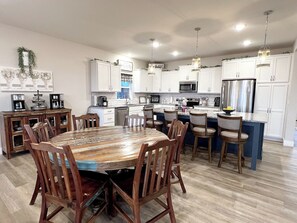 A modern kitchen with white cabinets, a central island, and a dining area with wooden chairs. - Blue Horizon-Panoramic Lake View on Indian Point (Branson)