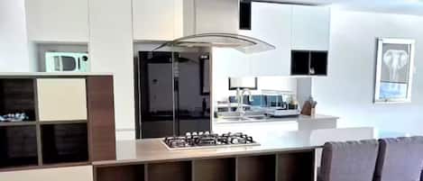 A modern kitchen with a central island, built-in appliances, and a dining area with chairs.