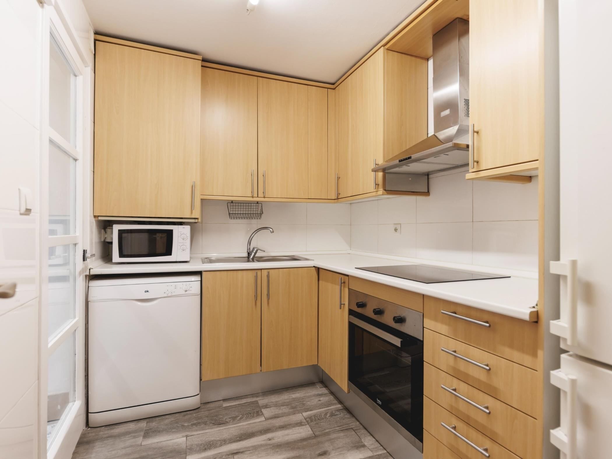 Una cocina compacta con armarios de madera, microondas, lavavajillas, fregadero y estufa.