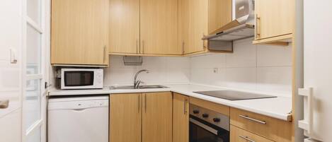 Una cocina compacta con armarios de madera, microondas, lavavajillas, fregadero y estufa.