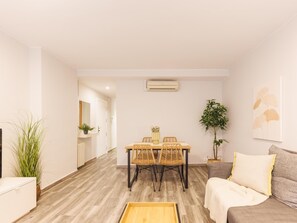 A modern living room with a sofa, a dining table with chairs, a coffee table, and a potted plant.