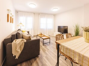 A modern living room with a sofa, a coffee table, a TV, and a dining area with a table and chairs. - Bravissimo Pons i Martí Baix, 1-bedroom apartment (Girona)