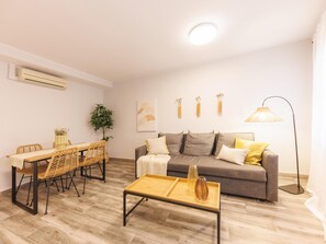 A living room with a sofa, a dining table with chairs, a floor lamp, and a small table with a vase. - Bravissimo Pons i Martí Baix, 1-bedroom apartment (Girona)