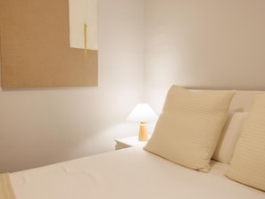 A bedroom with a bed, pillows, a nightstand, a lamp, and a wall-mounted item.