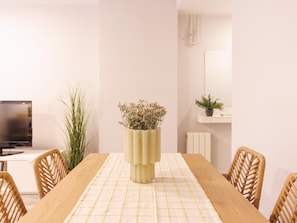 A dining area with a table set for four, a television on the left, and a potted plant on the right.